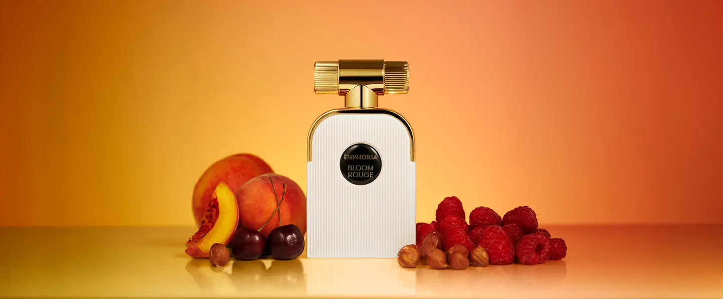 Bloom Rouge parfum bottle with peaches, cherries, raspberries and hazelnuts on a warm orange background